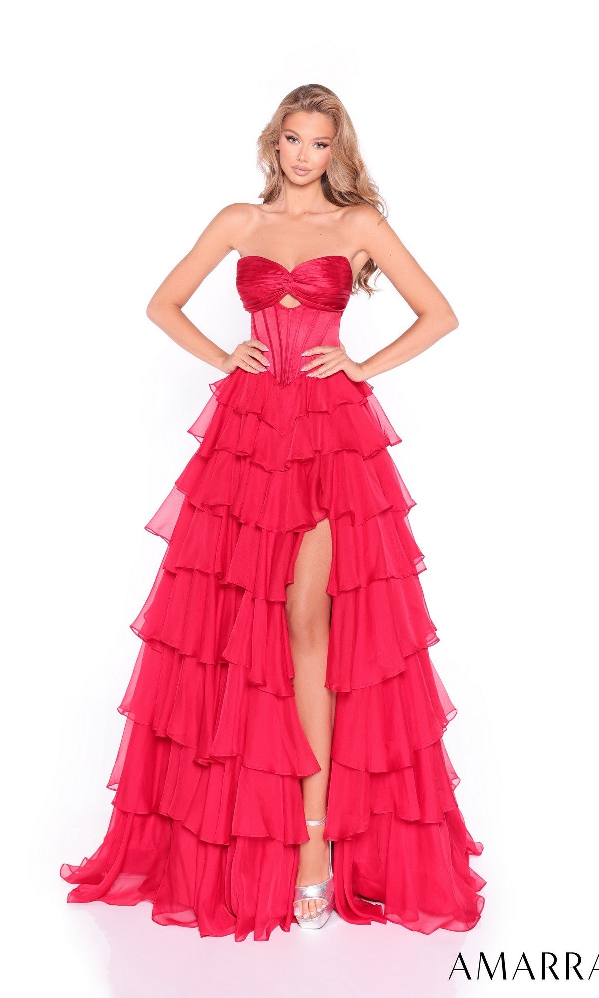 A woman wears the Amarra 89311 long prom dress featuring a strapless corset bodice, layered red chiffon A-line skirt with a high slit, and silver heels, posed against a plain white background.